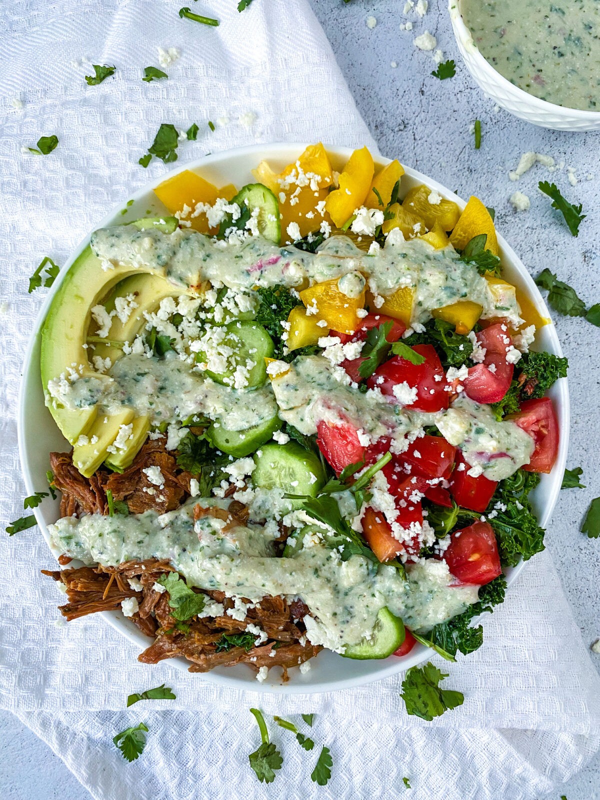 picture of prepared pulled pork bowl w/ cilantro maple dressing. a small bowl of dressing in the top corner of the photo as embellishment.